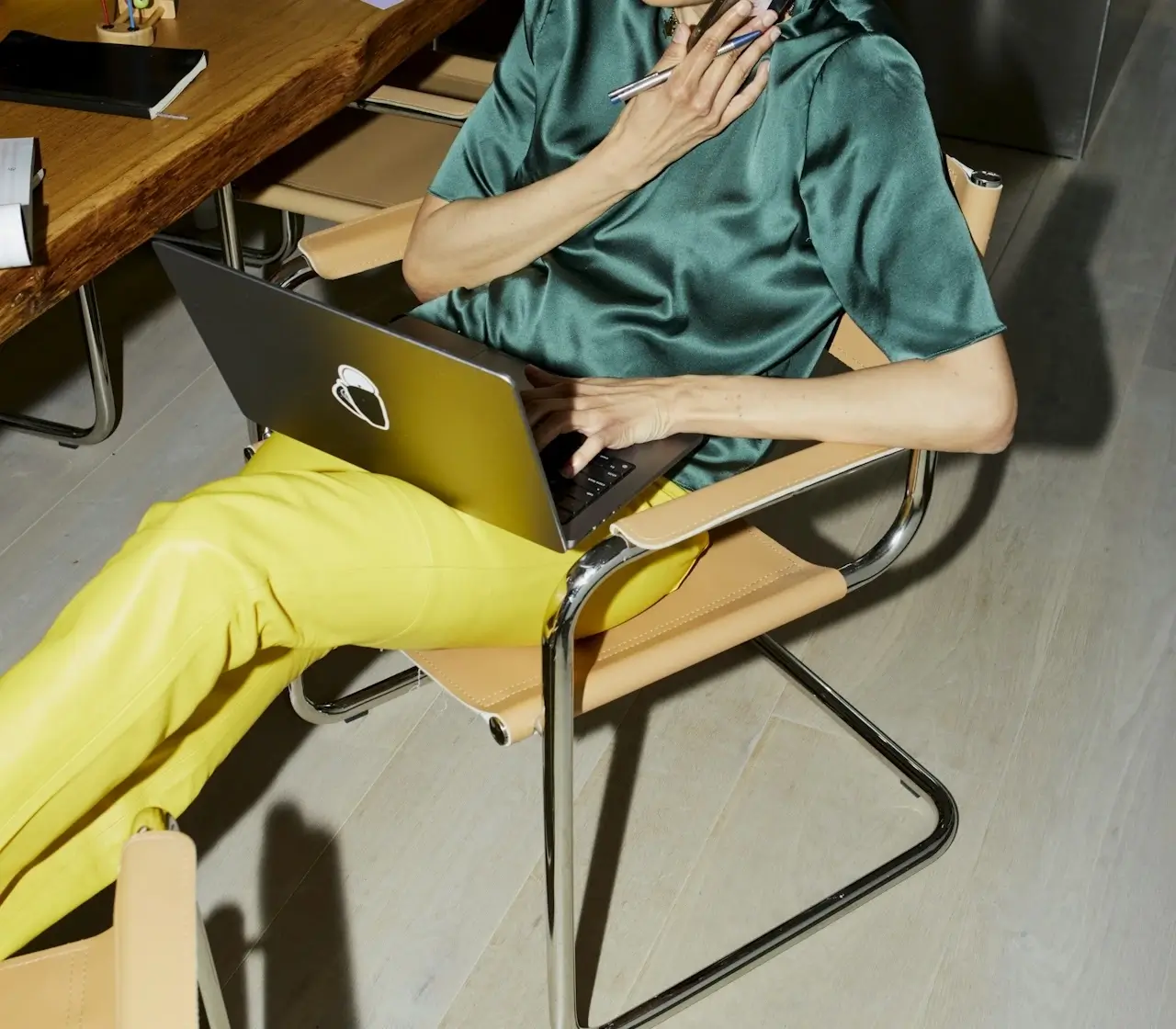 Kvinde i farverige bukser og silkebluse arbejder fokuseret på laptop – klar til at designe en hjemmeside, der ikke bare er pæn, men sælger.